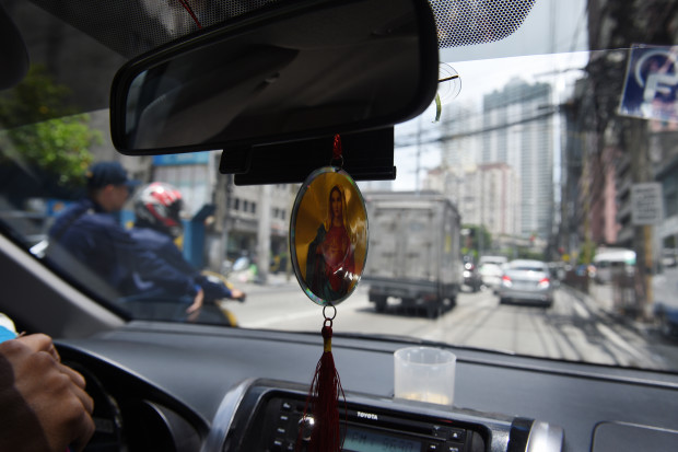 A Filipino taxi driver displays a religious icon inside his vehicle in Manila on May 22, 2017.  Philippine authorities have banned hanging rosaries and religious icons off car dashboards because of safety concerns, prompting an outcry from the Catholic Church which insists they offer divine intervention on the nation's chaotic roads. The ban, which will take effect on May 26, is part of a wide-ranging new law aimed at eliminating distractions for drivers.  / AFP PHOTO / Ted ALJIBE
