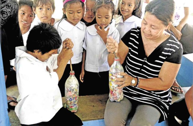 A parent demonstrates to students how to fill plastic bottles with wastes to be used as construction material for the only children’s library of Cobrador Island in Romblon province. —TEDDY PELAEZ