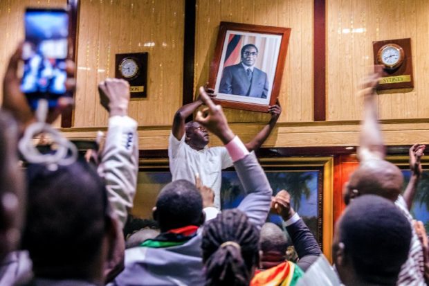 People remove, from the wall at the International Conference centre, where parliament had their sitting, the portrait of former Zimbabwean President Robert Mugabe after his resignation on November 21, 2017 in Harare. Robert Mugabe resigned as president of Zimbabwe on November 21, 2017 swept from power as his 37-year reign of brutality and autocratic control crumbled within days of a military takeover. The bombshell news was delivered by the parliament speaker to a special joint session of the assembly which had convened to impeach Mugabe, 93, who has dominated every aspect of Zimbabwean public life since independence in 1980.  / AFP PHOTO / Jekesai NJIKIZANA