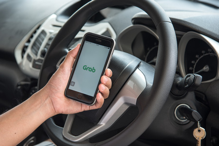 Man holding cellphone showing Grab logo.