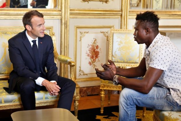 French President Emmanuel Macron (L) speaks with Mamoudou Gassama, 22, from Mali, at the presidential Elysee Palace in Paris, on May, 28, 2018. Mamoudou Gassama living illegally in France is being honored by Macron for scaling an apartment building over the weekend to save a 4-year-old child dangling from a fifth-floor balcony. / AFP PHOTO / POOL / Thibault Camus