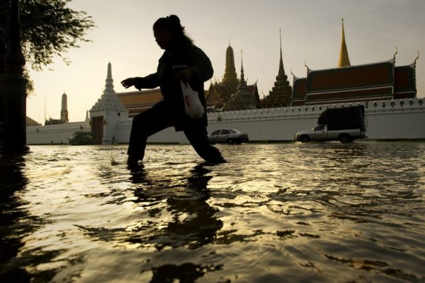 (FILES) This file photo taken on October 28, 2011 shows a woman walking through floodwaters in front of the Grand Palace near the Chao Praya river in Bangkok, when the year's monsoon season brought the worst floods in decades with a fifth of the city under water.  As Bangkok prepares to host climate change talks beginning September 4, 2018, the sprawling city of more than 10 million is itself under siege from the environment, with dire forecasts that it could be partially submerged in just over a decade. / AFP PHOTO / Nicolas ASFOURI / TO GO WITH Thailand environment climate economy FOCUS by Sophie DEVILLER
