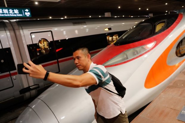 A passenger takes a selfie next to the first train of the Guangzhou-Shenzhen-Hong Kong Express Rail Linkas after it arrived in Shenzhen on September 23, 2018. A new high-speed rail link between Hong Kong and mainland China launched on September 23, a multi-billion dollar project that critics say gives away part of the city's territory to an increasingly assertive Beijing. / AFP PHOTO / POOL / TYRONE SIU