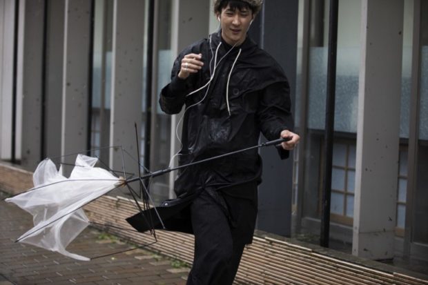 A pedestrian holds his broken umbrella a s he walks against a strong wind after Typhoon Trami hit the city of Kagoshima, on Kyushu island, on September 30, 2018. A powerful typhoon hurtled toward Japan's mainland after injuring dozens on southern islands, as weather officials warned that fierce winds and torrential rain could trigger landslides and floods.   / AFP PHOTO / Behrouz MEHRI