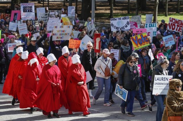 People hold signs next to women dressed as characters from "The Handmaid's Tale"  during a rally and march at Grant Park on October 13, 2018 in Chicago, Illinois to inspire voter turnout ahead of midterm polls in the United States. - Women angered by the bitter fight over a US Supreme Court nominee and what they called the "anti-woman agenda" of the Trump administration headed into the streets of Chicago on Saturday in a display of political might. The rally, organized by Women's March Chicago, was designed to spotlight the power and determination of women voters ahead of the crucial November 6 midterm elections, which will determine control of the US Congress. The elections are also being seen as a barometer of President Donald Trump's popularity. (Photo by Kamil Krzaczynski / AFP)