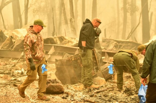 Yuba and Butte County Sheriff officers react as they discover a body at a burned out residence after the Camp fire tore through the area in Paradise, California, on November 10, 2018. - Firefighters in California on November 10 battled raging blazes at both ends of the state that have left at least nine people dead and thousands of homes destroyed, but there was little hope of containing the flames anytime soon. So far, all nine fatalities were reported in the town of Paradise, in Butte County, where more than 6,700 buildings, most of them residences, have been consumed by the late-season inferno, which is now California's most destructive fire on record. (Photo by Josh Edelson / AFP)