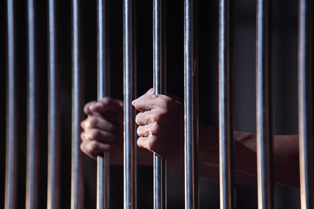 Stock photo of hands holding jail bars