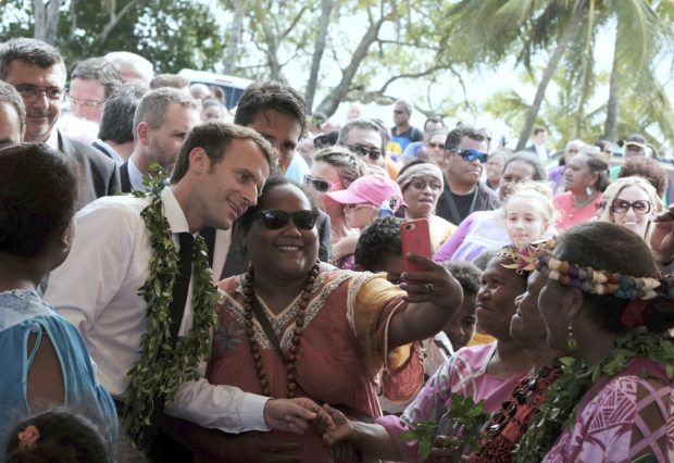 FILE - In this Saturday, May 5, 2018 file photo French President Emmanuel Macron, left, poses for a selfie while meeting residents as part of a remembrance ceremony on the Ouvea Island, off New Caledonia. New Caledonia, a French archipelago in the South Pacific, is preparing for an independence referendum upcoming Sunday Nov. 4, 2018, the last step in a three-decades-long decolonization effort. (AP Photo/Theo Rouby, File)