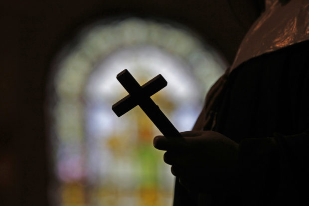FILE - This Dec. 1, 2012 file photo shows a silhouette of a crucifix and a stained glass window inside a Catholic Church in New Orleans. As U.S. Catholic bishops gather for an important national assembly, the clergy sex abuse crisis dominates their agenda. But it's only one of several daunting challenges facing the nation's largest religious denomination. While federal and state law enforcement agencies widen their investigations of abuse, the church finds itself with ever fewer priests and nuns in service. (AP Photo/Gerald Herbert)