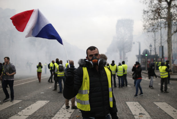 A demonstrator waves a French flag on the Champs-Elysees avenue Saturday, Dec. 8, 2018 in Paris. Crowds of yellow-vested protesters angry at President Emmanuel Macron and France's high taxes tried to converge on the presidential palace Saturday, some scuffling with police firing tear gas, amid exceptional security measures aimed at preventing a repeat of last week's rioting. (AP Photo/Rafael Yaghobzadeh) paris