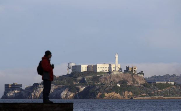 A man stands on a pier with Alcatraz Island at rear in San Francisco, Saturday, Dec. 22, 2018. A partial federal shutdown has been put in motion because of gridlock in Congress over funding for President Donald Trump's Mexican border wall. The company that provides ferry services to Alcatraz Island kept its daytime tours but canceled its behind-the-scenes and night tours for Saturday. (AP Photo/Jeff Chiu)