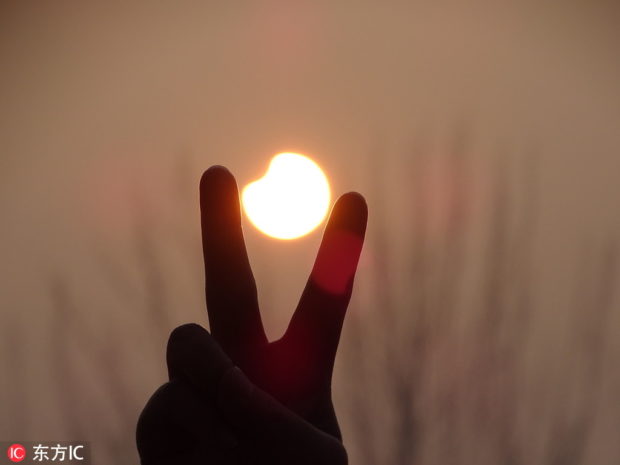 A local in Zoucheng, East China's Shandong province, makes the V-sign before the partially eclipsed sun on Sunday morning. IC via China Daily/Asia News Network