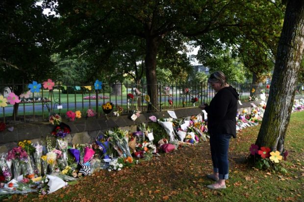 A woman writes a note to leave among flowers left in tribute to victims in Christchurch on March 17, 2019, two days after a shooting incident at two mosques in the city. - The death toll from horrifying shootings at two mosques in New Zealand rose to 50, police said Sunday, as Christchurch residents flocked to memorial sites and churches across the city to lay flowers and mourn the victims. (Photo by Anthony WALLACE / AFP)