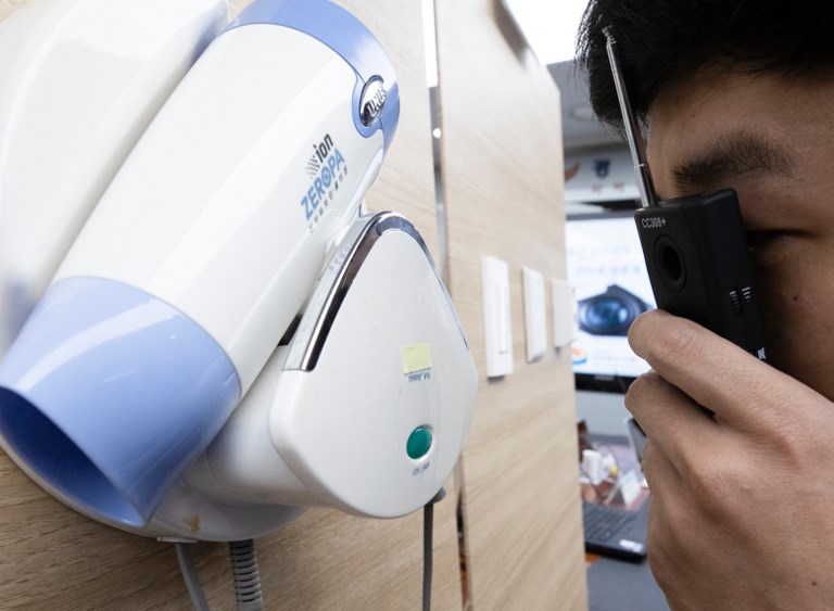 This picture taken on March 20, 2019 shows a police official testing a detector in front of a hidden mini-camera installed in a hair-dryer holder as South Korean police talk to the media about the latest spycam-related crime at the Korean National Police Agency in Seoul. - More than 800 South Korean couples were livestreamed having sex in love motels, Seoul police said Thursday in one of the largest-scale and most intrusive examples yet of the country's spycam epidemic. (Photo by - / YONHAP / AFP) / - South Korea OUT / REPUBLIC OF KOREA OUT  NO ARCHIVES  RESTRICTED TO SUBSCRIPTION USE