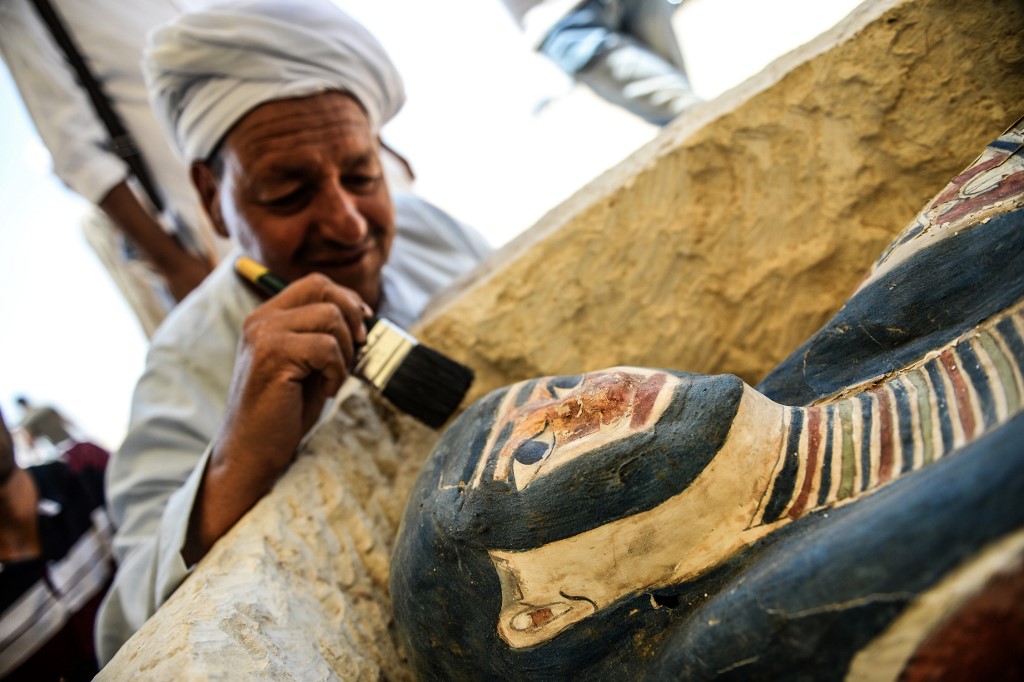 A man brushes off dust from a sarcophagus, part of a new discovery carried out almost 300 meters south of King Amenemhat IIs pyramid at Dahshur necropolis, exposed near the Bent Pyramid, about 40km (25 miles) south of the Egyptian capital Cairo, during an inaugural ceremony of the pyramid and its satellites, on July 13, 2019. - An Egyptian archaeological mission discovered a collection of stone, clay and wooden sarcophagi, of which some are still containing well preserved mummies, as well as a collection of wooden funerary masks and instruments used in cutting stones . (Photo by Mohamed el-Shahed / AFP)