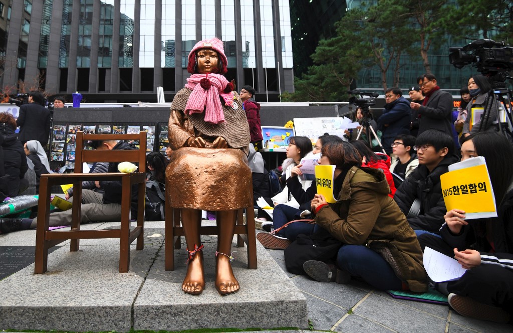 South Korean protesters sit near a statue of a teenage girl symbolizing former "comfort women", who served as sex slaves for Japanese soldiers during World War II, during a weekly anti-Japanese demonstration in front of the Japanese embassy in Seoul on November 21, 2018. - South Korea on November 21 announced the formal shutdown of a controversial Japanese-funded foundation created to help former wartime sex slaves -- a move that will further sour ties between the neighbours. (Photo by Jung Yeon-je / AFP)