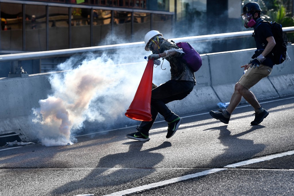(FILES) This file photo taken on August 5, 2019 shows a protester preparing to cover a tear gas canister fired by the police with a traffic cone in the Admiralty district of Hong Kong during a general strike, as simultaneous rallies were held across seven districts. - Hong Kong protesters who have taken to the streets for nearly two months are harnessing everything from traffic cones to kitchenware to battle tear gas as demonstrations escalate. (Photo by Anthony WALLACE / AFP) / TO GO WITH HongKong-politics-China-unrest-police,FOCUS