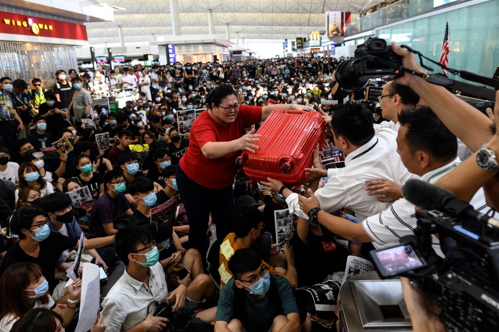 A tourist (C) gives her luggage to security guards as she tries to enter the departures gate during another demonstration by pro-democracy protesters at Hong Kong's international airport on August 13, 2019. - Protesters blocked passengers at departure halls of Hong Kong airport on August 13, a day after a sit-in forced authorities to cancel all flights to and from the major international hub. (Photo by Philip FONG / AFP)