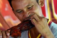 This photo taken on August 8, 2019 shows a man eating a grilled rat at a stall in Battambang province. - Barbecued field rats are not everybody's idea of a tasty treat, but in Cambodia's rural Battambang province they are popular as a cheap - and quick - snack, with small skewered ones going for 0.25USD each while larger rodents can cost 1.25USD. (Photo by TANG CHHIN Sothy / AFP)