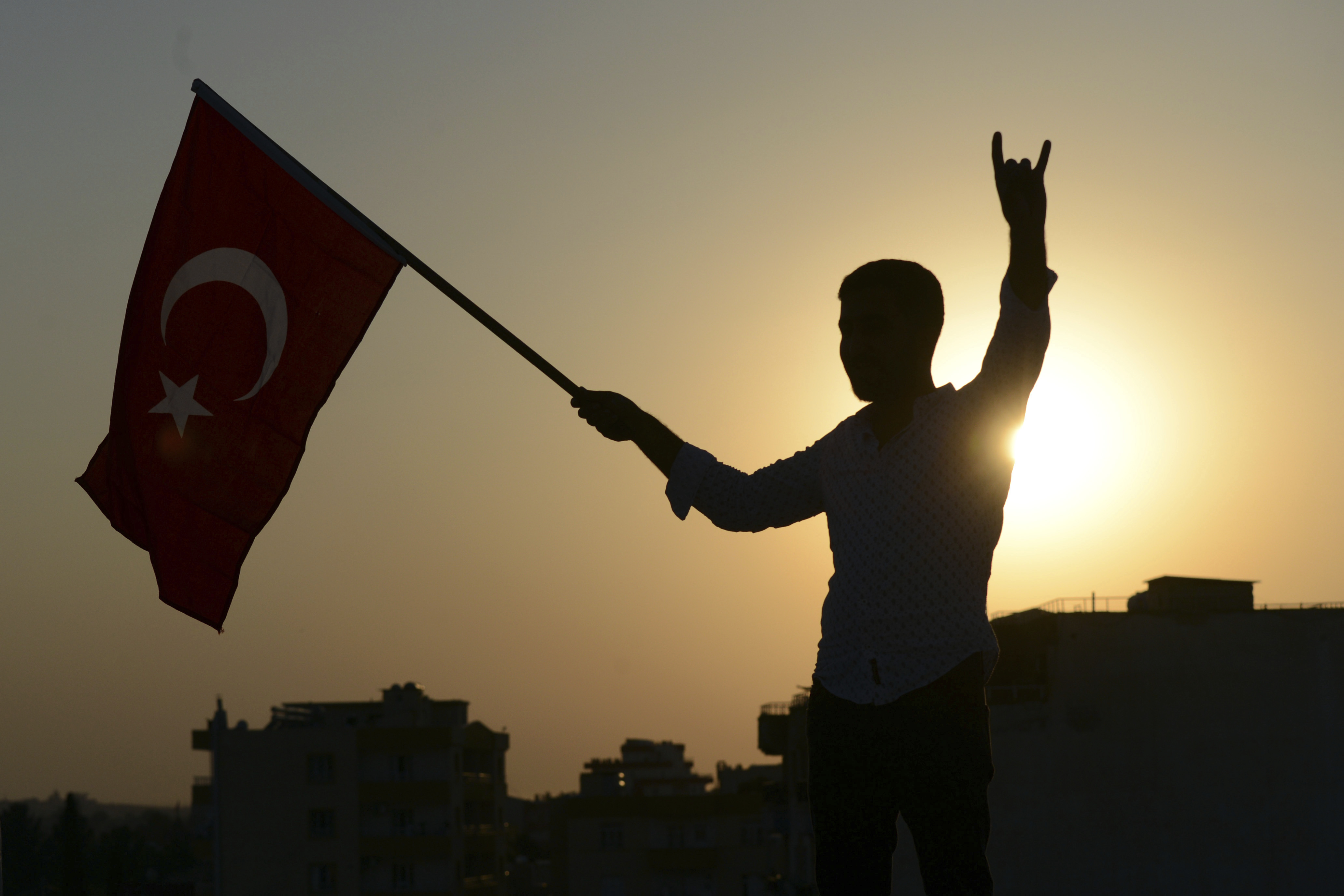 A Turkish youth celebrates with a national flag after news about Syrian town of Tal Abyad, in Turkish border town of Akcakale, in Sanliurfa province, Sunday, Oct. 13, 2019. Turkey's official Anadolu news agency, meanwhile, said Turkey-backed Syrian forces have advanced into the center of a Syrian border town, Tal Abyad, on the fifth day of Turkey's military offensive. (Ismail Coskun/IHA via AP)