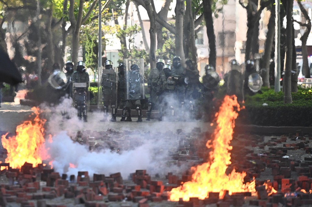 Riot police look on as fires from molotov cocktails, thrown by protesters, burn after police fired tear gas outside the Hong Kong Polytechnic University in Hong Kong on November 17, 2019. - Hong Kong police fired tear gas on November 17 morning at protesters intent on keeping their stranglehold on a major tunnel as pro-democracy activists vowed to "squeeze the economy" into next week. (Photo by Philip FONG / AFP)