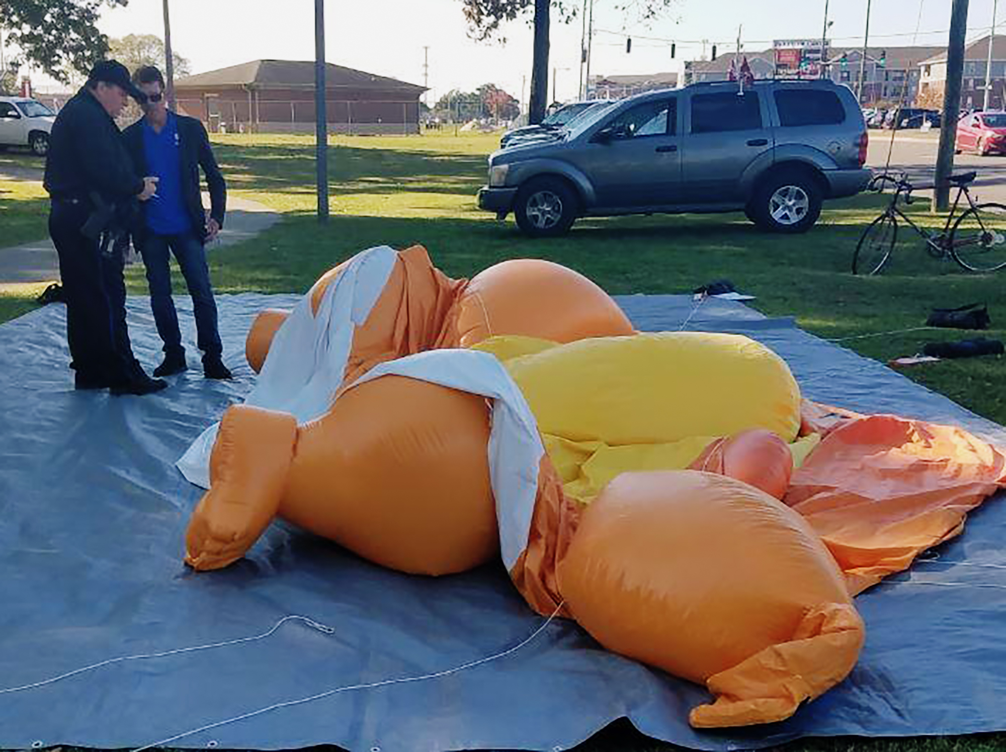 A responding officer and an unidentified man stands by a Baby Trump balloon deflated by someone at Monnish Park as people were protesting President Donald Trump's visit to an NCAA college football game between Louisiana State and Alabama playing nearby in Tuscaloosa, Ala., Saturday, Nov. 9, 2019. The towering Baby Trump protest balloon was knifed and deflated by someone unhappy with its appearance during Trump's trip to Alabama, organizers said. (Stephanie Taylor/The Tuscaloosa News via AP)