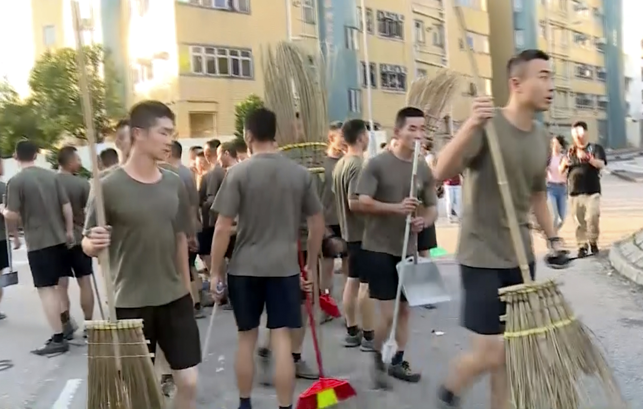 In this image made from video, People’s Liberation Army soldiers, with brooms, arrive to clean up the protest area at Hong Kong Baptist University in Hong Kong, Saturday, Nov. 16, 2019. Troops from the Chinese army joined an effort to clean up debris outside the university, which was the site of clashes this week. (Television Broadcasts Limited Hong Kong via AP)