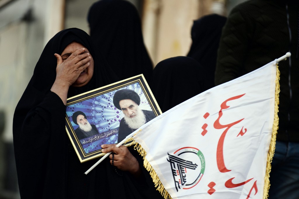 An  mourner carries a framed image of Iraq's top Shiite cleric Grand Ayatollah Ali Sistani as the coffins of slain Iraqi paramilitary chief Abu Mahdi al-Muhandis, Iranian military commander Qasem Soleimani and eight others towards the Imam Ali Shrine in the shrine city of Najaf in central Iraq during a funeral procession on January 4, 2020. - Thousands of Iraqis chanted "Death to America" today as they mourned the deaths of  al-Muhandis and Soleimani, who were killed in a US drone attack that sparked fears of a regional proxy war between Washington and Tehran. (Photo by Haidar HAMDANI / AFP)