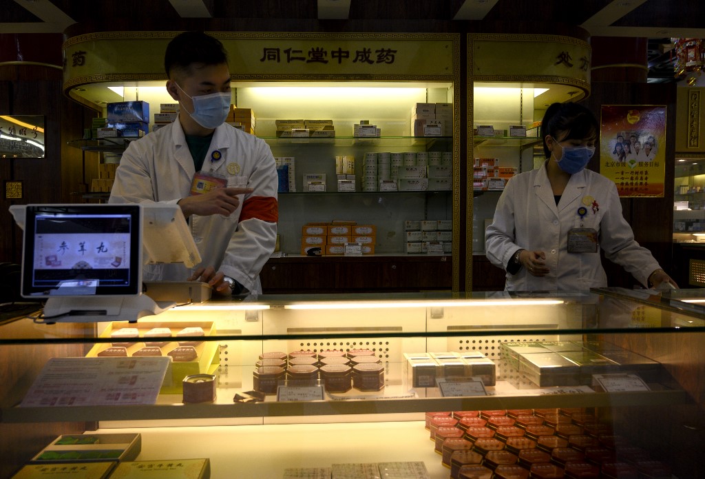 This photo taken on February 1, 2020 shows employees wearing protective face masks at a traditional Chinese medicine store in Beijing. - A claim by Chinese scientists that a liquid made with honeysuckle and flowering plants could help fight the deadly coronavirus has sparked frenzied buying of the traditional medicine, but doubts quickly emerged. (Photo by NOEL CELIS / AFP) / TO GO WITH China-health-virus-medicine,FOCUS