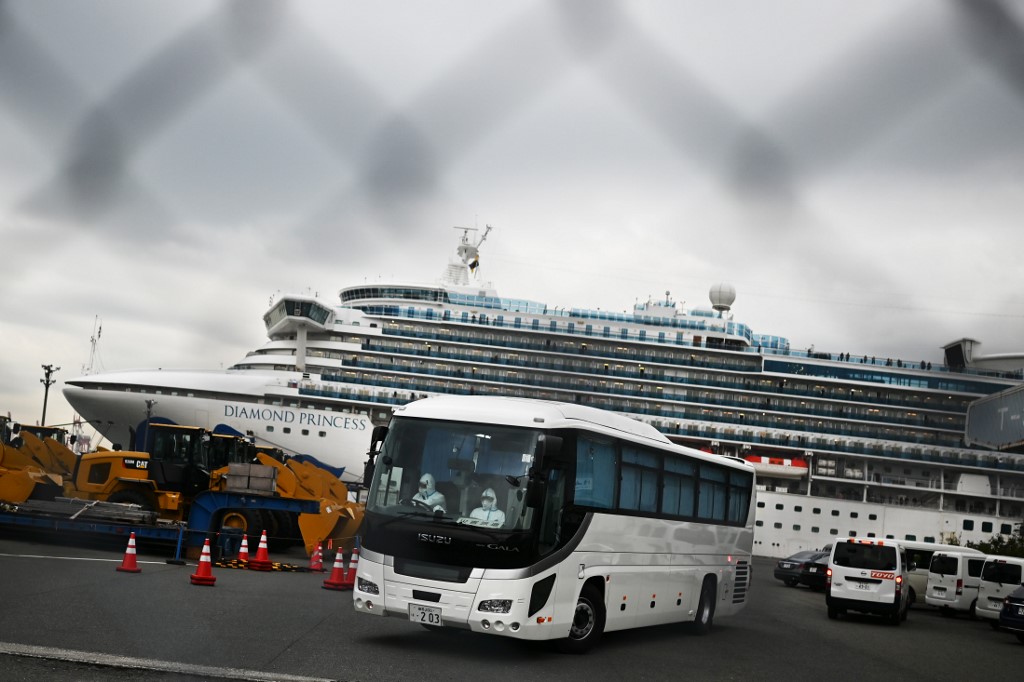 A bus with a driver (L) wearing protective gear departs from the dockside next to the Diamond Princess cruise ship, which has around 3,600 people quarantined onboard due to fears of the new COVID-19 coronavirus, at the Daikoku Pier Cruise Terminal in Yokohama port on February 14, 2020. - Japanese authorities were preparing Febraury 14 to move some older passengers who tested negative for the new coronavirus off a quarantined cruise ship and into government-designated lodging. (Photo by CHARLY TRIBALLEAU / AFP)