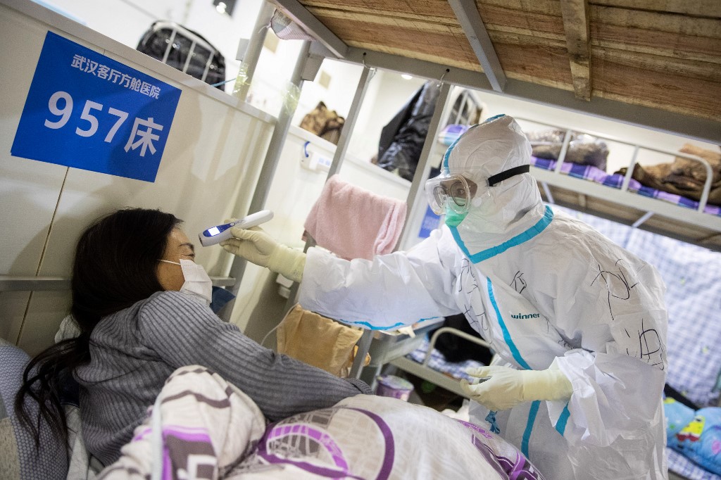 This photo taken on February 17, 2020 shows a member of the medical staff (L) checking the body temperature of a patient who has displayed mild symptoms of the COVID-19 coronavirus, at an exhibition centre converted into a hospital in Wuhan in China's central Hubei province. - The death toll from the COVID-19 coronavirus epidemic jumped to 1,868 in China on February 18 after 98 more people died, according to the National Health Commission. (Photo by STR / AFP) / China OUT
