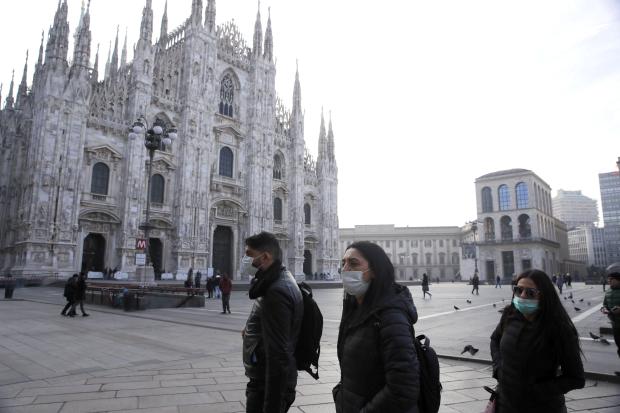 People in masks walking past Duomo cathedral in Milan