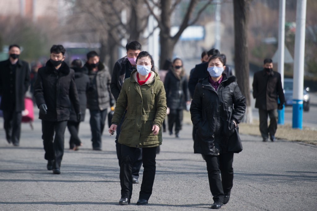 People wearing face masks walk down Kwangbok street in Pyongyang on February 26, 2020. - The novel coronavirus has killed over 2,700 people and infected more than 80,000 in 34 countries, although the vast majority of cases remain in China, according to the World Health Organization (WHO). (Photo by KIM Won Jin / AFP)