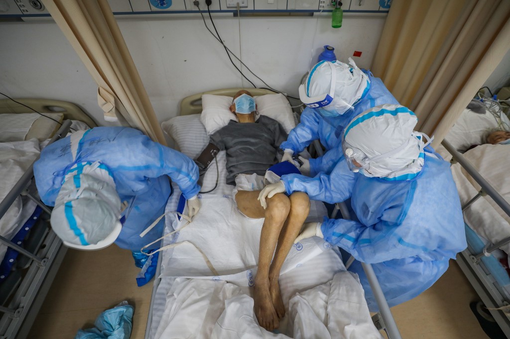 This photo taken on March 6, 2020 shows medical staff helping a COVID-19 coronavirus patient at the Red Cross hospital in Wuhan in China's central Hubei province. - China on March 7 reported 28 new deaths from the COVID-19 coronavirus outbreak, bringing the nationwide toll to 3,070. (Photo by STR / AFP) / China OUT