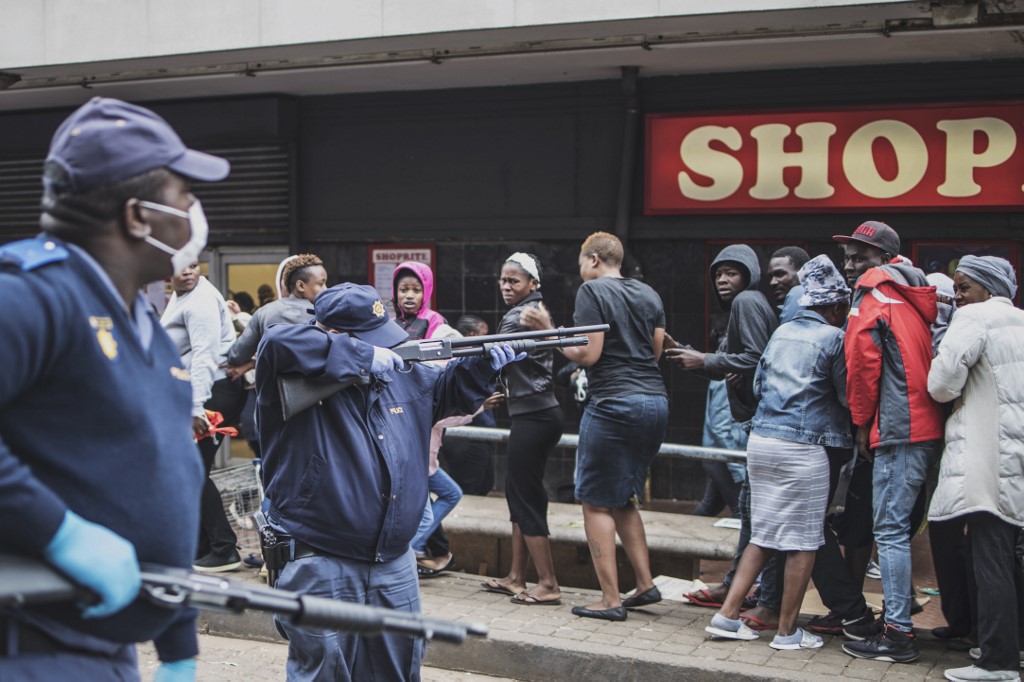 A South African policeman points his pump rifle to disperse a crowd of shoppers in Yeoville, Johannesburg, on March 28, 2020 while trying to enforce a safety distance outside a supermarket amid concern of the spread of COVID-19 coronavirus. - South Africa came under a nationwide lockdown on March 27, 2020, joining other African countries imposing strict curfews and shutdowns in an attempt to halt the spread of the COVID-19 coronavirus across the continent. (Photo by MARCO LONGARI / AFP)