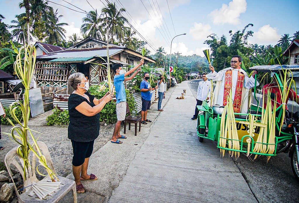 A Roman Catholic priest riding on a tricycle and wearing a face mask blesses the faithfuls holding coconut leaves during Palm Sunday event in Borongan town, Eastern Samar province, central Philippines on April 5, 2020, as part of the Easter observance. - Church authorities have asked the catholic faithfuls not to go to churches for the Palm Sunday blessing, but instead to stay in front of their houses as priests will go around their communities for the blessing, to observe social distancing as part of the government efforts to combat COVID 19 pandemic. (Photo by Alren BERONIO / AFP)