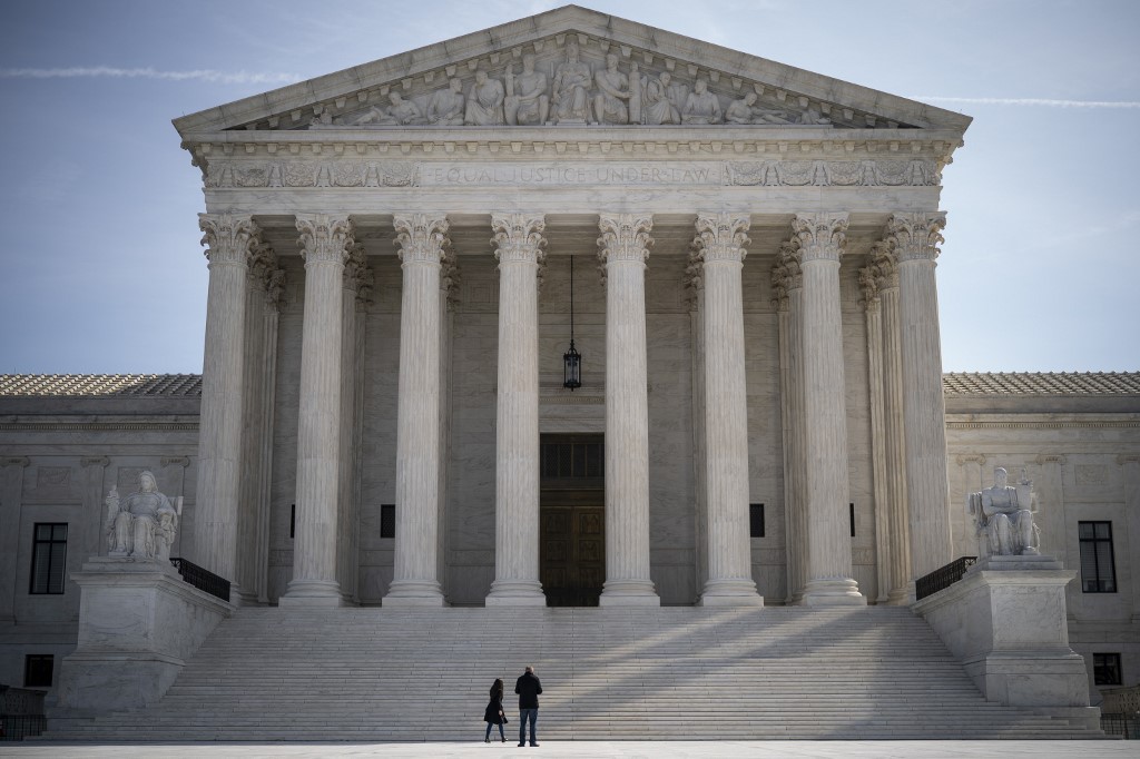 WASHINGTON, DC - MARCH 16: Two people stand at the base of the U.S. Supreme Court on March 16, 2020 in Washington, DC. The Supreme Court announced on Monday that it would postpone oral arguments for its March session because of the coronavirus outbreak.   Drew Angerer/Getty Images/AFP