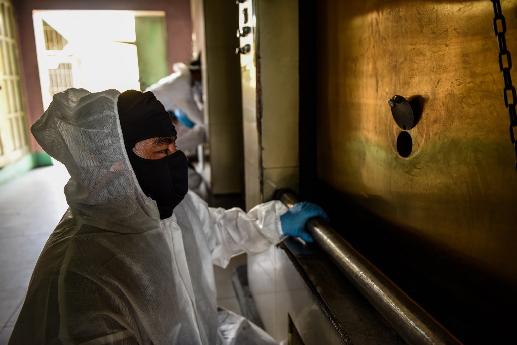 A worker in a protective suit, used due to the COVID-19 coronavirus outbreak, checks the cremation chamber through a small peephole in the furnace at a crematorium facility in Manila on April 29, 2020. - Most of the Philippines is under quarantine to contain the spread of the coronavirus that has infected over 7,000 people and killed at least 500 in the country. (Photo by Maria TAN / AFP)