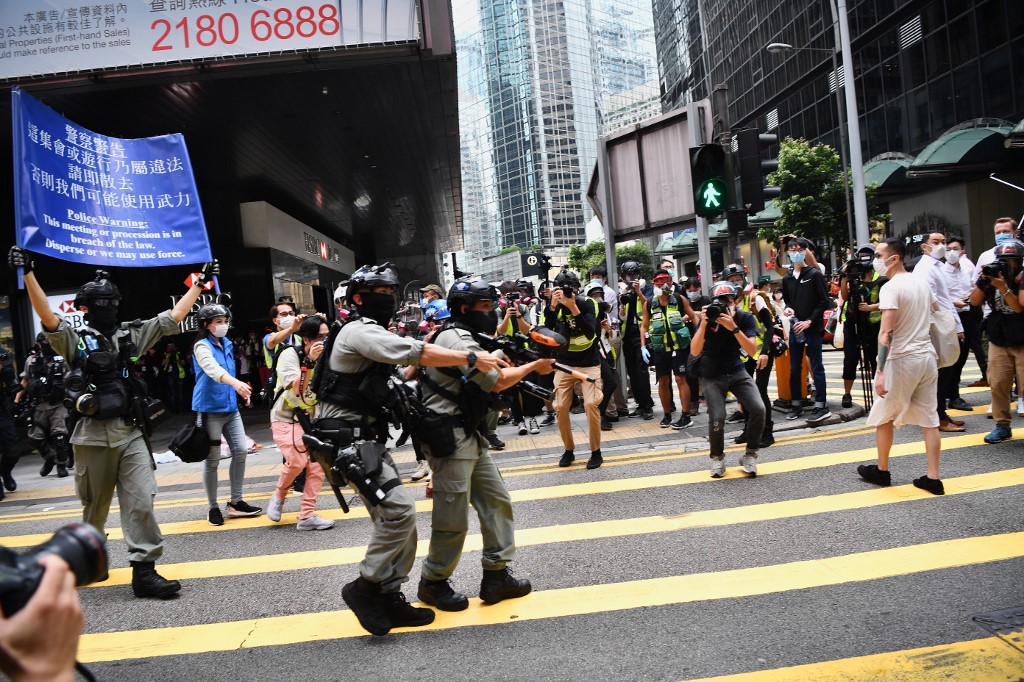 Hong Kong riot police (L) issue a warning as they plan to clear away people gathered in the Central district of downtown Hong Kong on May 27, 2020, as the city's legislature debates over a law that bans insulting China's national anthem. - A few hundred protesters chanted slogans during a lunchtime rally in the city's Central district but dispersed when officers fired multiple rounds of irritant-filled pellets, AFP reporters on the scene said. (Photo by Anthony WALLACE / AFP)