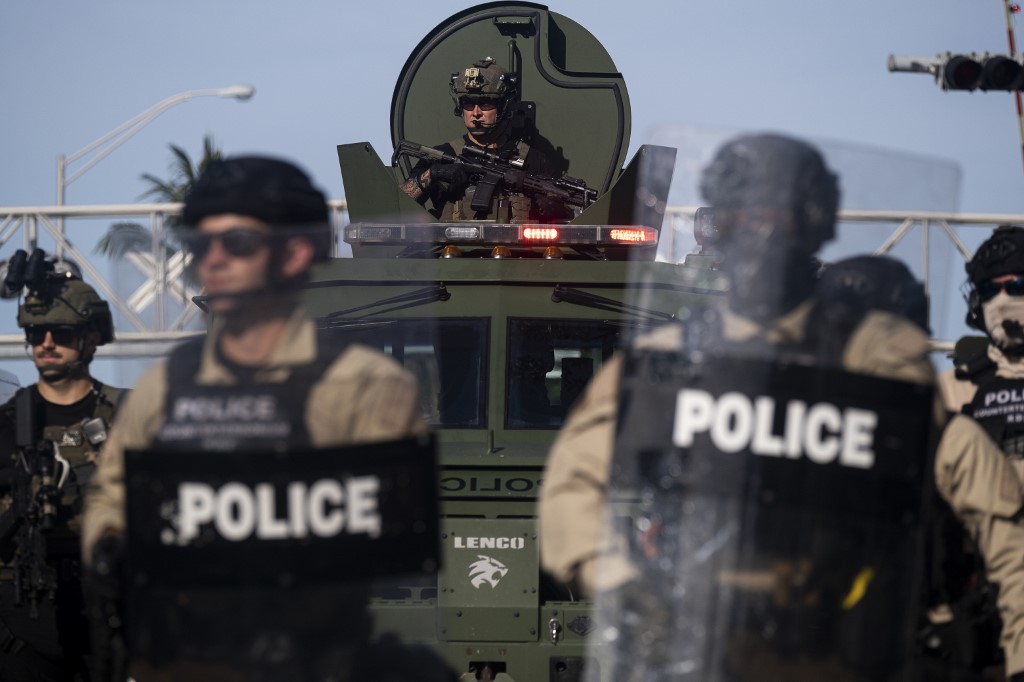 (FILES) In this file photo taken on May 31, 2020 a Miami Police officer watches protestors from a armored vehicle during a rally in response to the recent death of George Floyd in Miami, Florida. - When US police flooded the streets around the country to confront protesters two weeks ago, for many it appeared like the army had deployed, with camouflage uniforms and combat gear, heavily armored anti-mine vehicles, and high-powered assault weapons.  That's not by accident. For years the US Defense Department has been handing its surplus equipment over for free to police departments -- and the departments, large and small, have revelled in it. (Photo by Ricardo ARDUENGO / AFP)