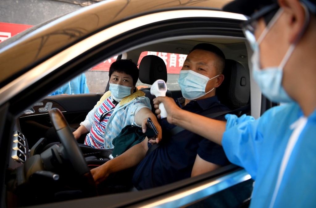 A security personnel wearing a protective suit checks the temperature of people entering the Xinfadi market in Beijing on June 14, 2020. - The domestic outbreak in China had been brought largely under control through strict lockdowns that were imposed early this year -- but a new cluster has been linked to Xinfadi market in south Beijing. (Photo by NOEL CELIS / AFP)