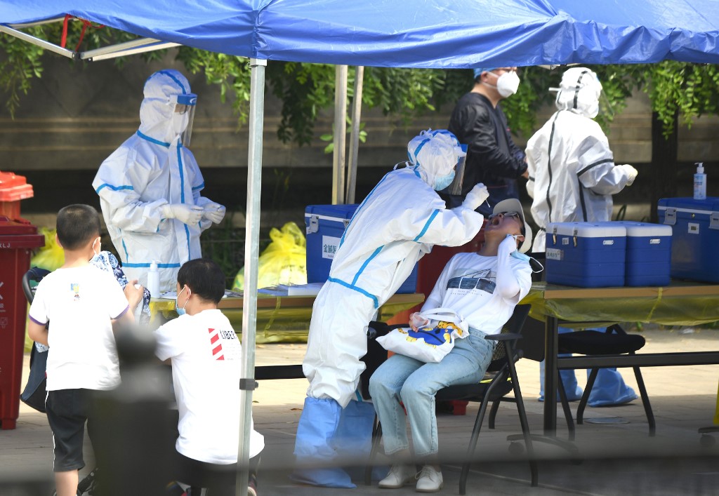 A health worker (2nd-L) wearing a protective suit takes a swab test on a woman in Beijing on June 16, 2020. - China reported another 27 domestically transmitted coronavirus cases in Beijing, where a fresh cluster linked to a wholesale food market has sparked WHO concern and prompted a huge trace-and-test programme. (Photo by Noel Celis / AFP)