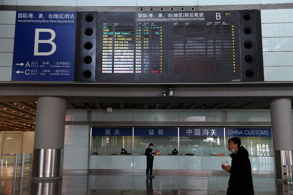 (FILES) This file photo taken on March 27, 2020 shows people standing below a board showing international arrivals, in the empty arrivals area at Beijing Capital Airport. - Beijing cancelled at least 1,255 scheduled inbound and outbound flights on June 17, 2020 as fears grow over a new virus outbreak, affecting nearly 70 per cent of all trips, reported the state-run media. (Photo by GREG BAKER / AFP)
