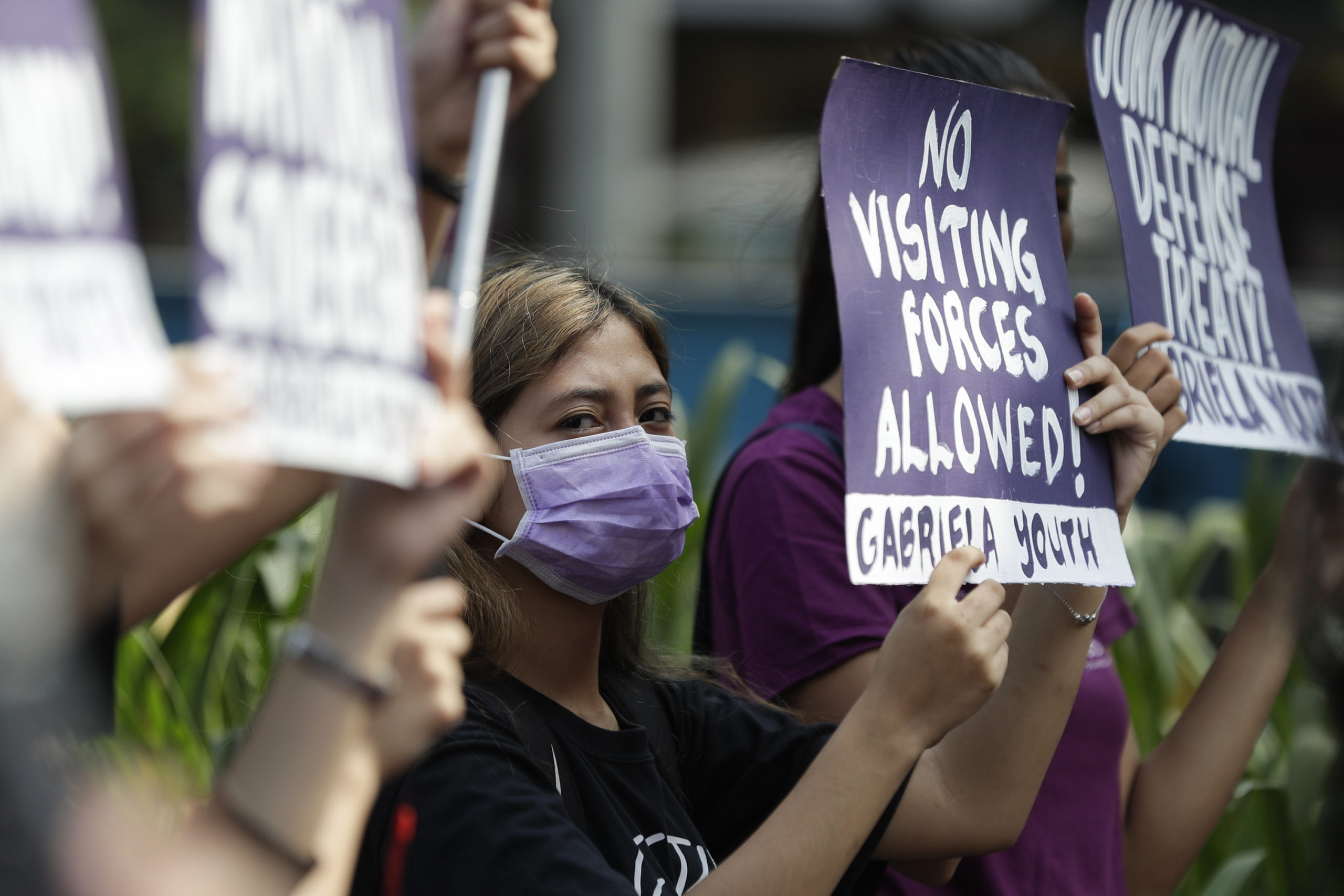 FILE - In this March 6, 2020, file photo, a woman protester wearing a protective mask holds a slogan during a rally outside the U.S. Embassy in Manila, Philippines against the planned military exercises between the Philippines and US under the Visiting Forces Agreement. The Philippines has decided not to suspend a defense pact with the U.S., avoiding a major blow to one of America’s oldest alliances in Asia.(AP Photo/Aaron Favila, File)