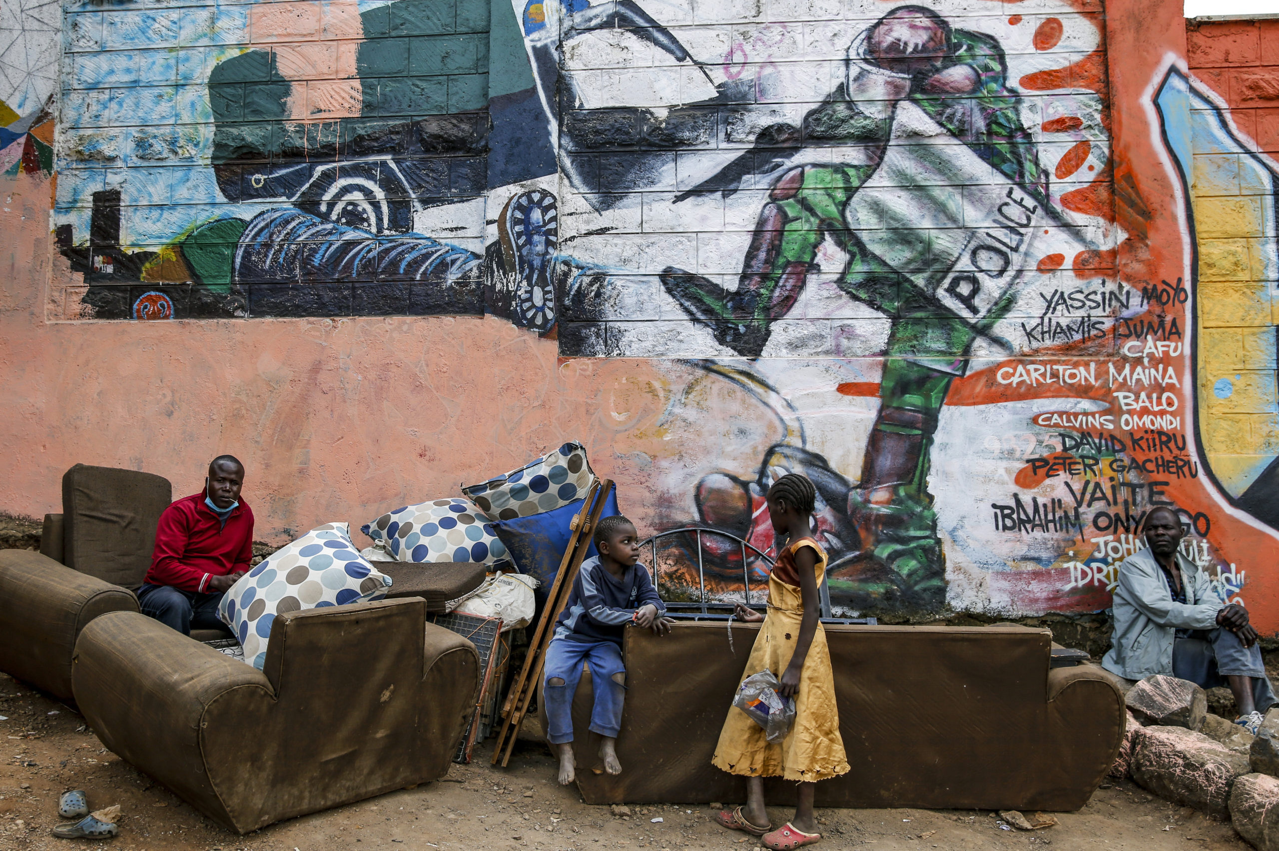 FILE - In this June 9, 2020, file photo, Kenyan children and men are photographed in the Kibera slum in Nairobi, Kenya, in front of a new mural showing an incident in 2016 when a Kenyan riot policeman repeatedly kicked a protester. The killing of George Floyd in the United States has raised awareness over police violence in South Africa and Kenya. (AP Photo/Brian Inganga, File)