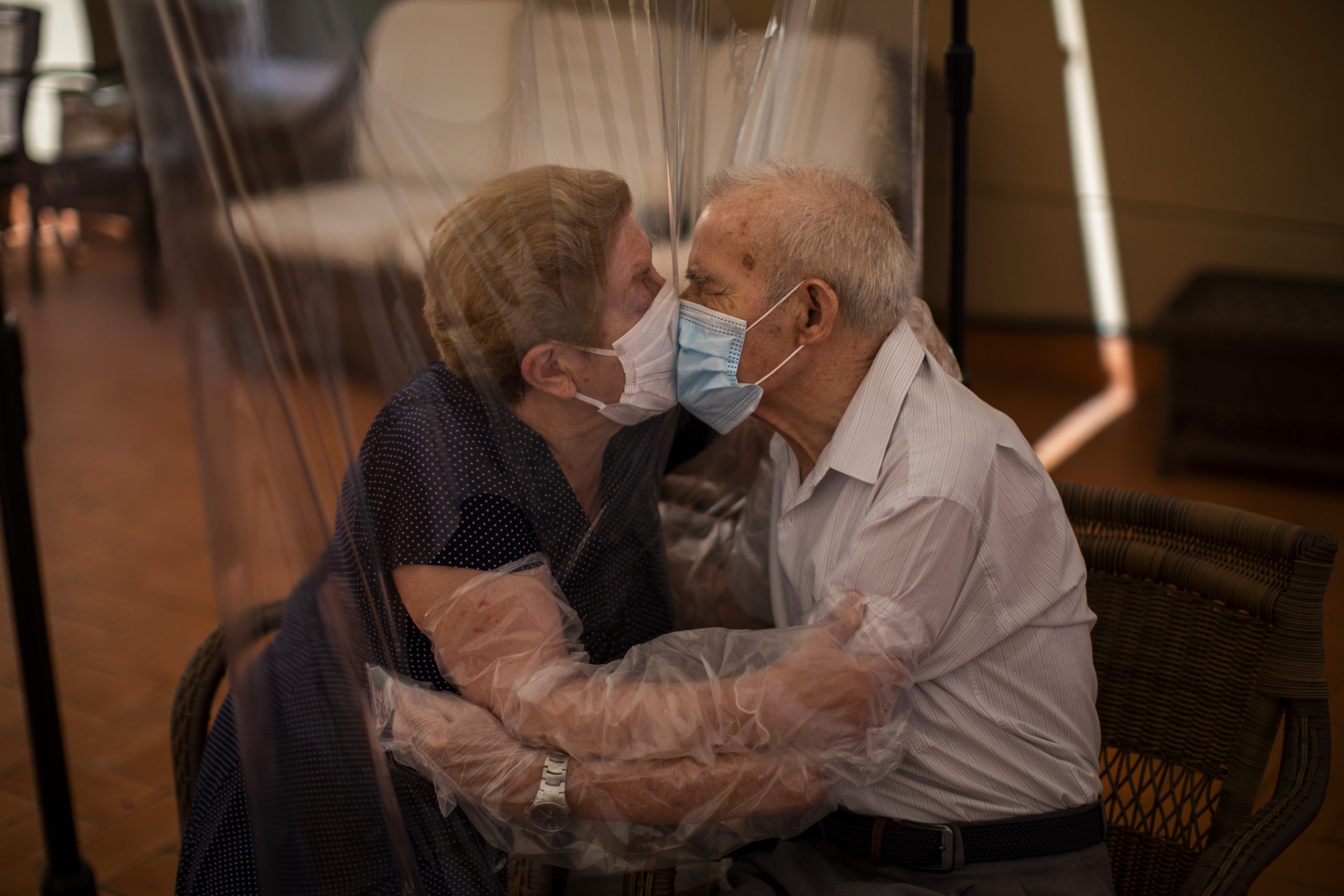 In this Monday, June 22, 2020 photo, Agustina Cañamero, 81, and Pascual Pérez, 84, hug and kiss through a plastic film screen to avoid contracting the new coronavirus at a nursing home in Barcelona, Spain. Even when it comes wrapped in plastic, a hug can convey tenderness and relief, love and devotion. The fear that gripped Agustina Cañamero during the 102 days she and her 84-year-old husband spent physically separated during Spain's coronavirus outbreak dissolved the moment the couple embraced through a screen of plastic film. (AP Photo/Emilio Morenatti)