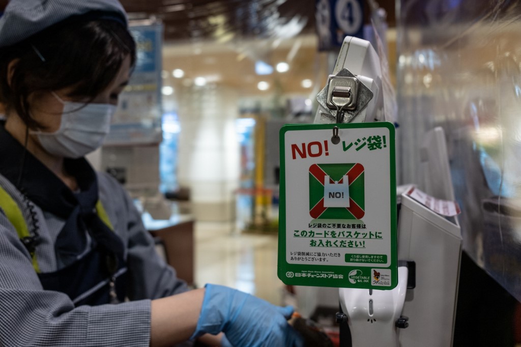 This photo taken on June 24, 2020 shows a cashier standing next to a sign reading "No shopping bag" to encourage customers to use fewer plastic bags at a supermarket in Tokyo. - Retailers in Japan began charging for plastic bags on July 1, a move aimed at curbing Japanese consumers' love for packaging and finally bringing the country in line with other major economies. (Photo by Philip FONG / AFP)