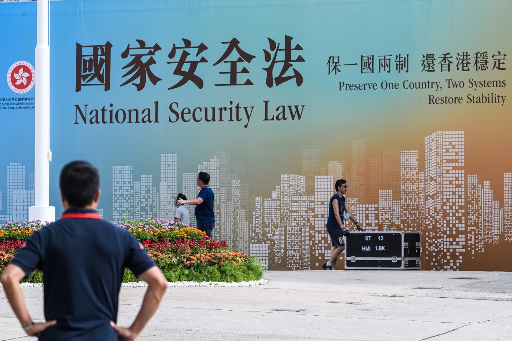 Technicians walk next to a banner supporting the new national security law at the end of a flag-raising ceremony to mark the 23rd anniversary of Hong Kong's handover from Britain in Hong Kong on July 1, 2020. - Hong Kong marked the 23rd anniversary of its handover to China on July 1 under the glare of a new national security law imposed by Beijing, with protests banned and the city's cherished freedoms looking increasingly fragile. (Photo by Anthony WALLACE / AFP)