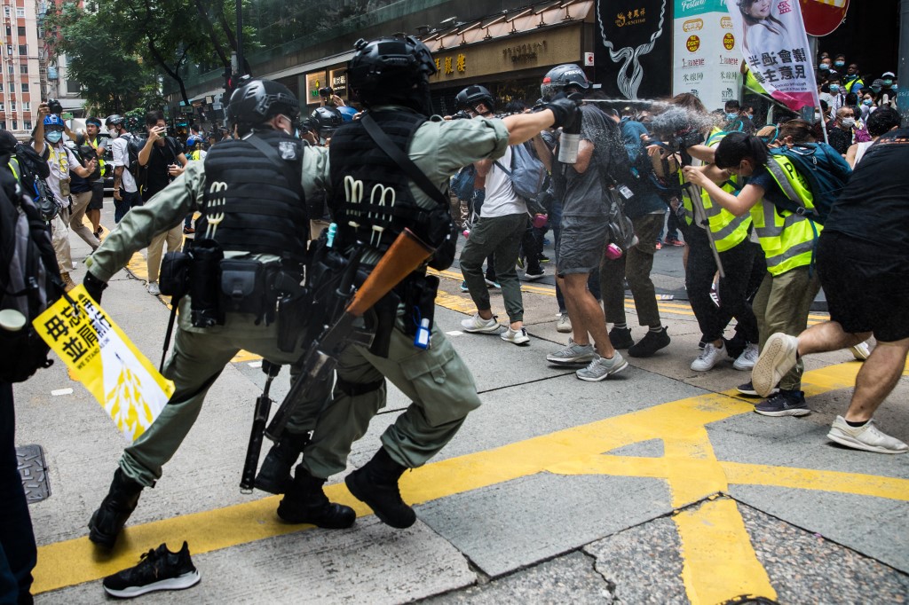 Riot police (L) deploy pepper spray toward journalists (R) as protesters gathered for a rally against a new national security law in Hong Kong on July 1, 2020, on the 23rd anniversary of the city's handover from Britain to China. - A man found in possession of a Hong Kong independence flag became the first person to be arrested under Beijing's new national security law for the city, police said on July 1. (Photo by DALE DE LA REY / AFP)