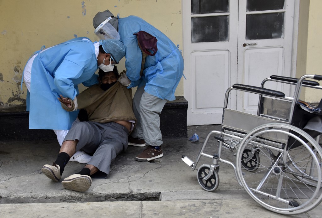 Health workers help a patient allegedly infected with the new coronavirus, get on a wheelchair in the yard of the Clinics Hospital in La Paz on July 23, 2020. (Photo by AIZAR RALDES / AFP)